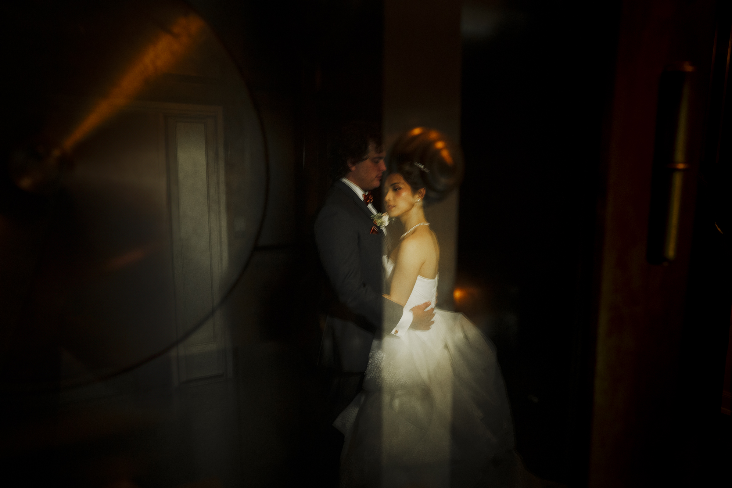 A bride and groom embrace in a dimly lit room at Duke Chapel. The bride, in her white gown, and the groom, in his dark suit, are enveloped by a soft glow, creating a romantic and dreamlike atmosphere.