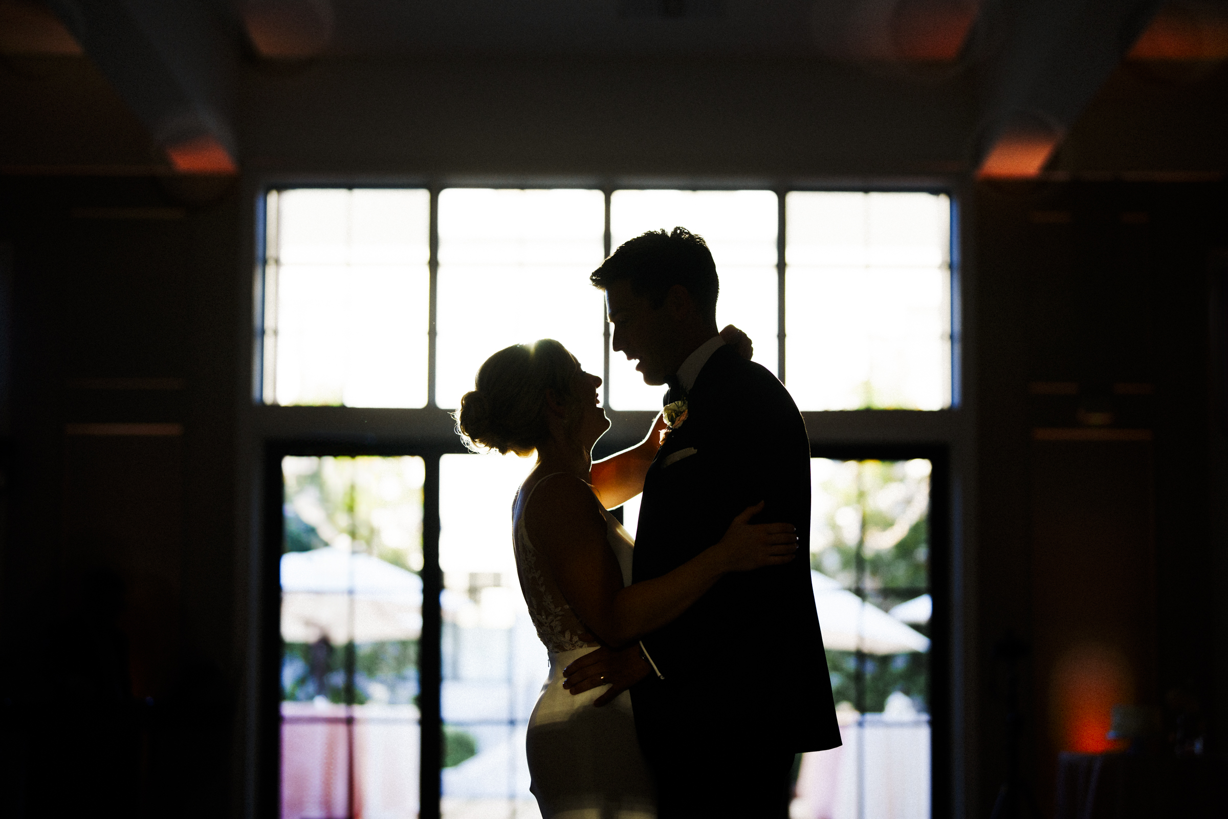 Silhouetted couple dancing closely at The Bradford Wedding, embraced under soft lighting near large windows. Their outlines are highlighted by daylight streaming in, creating a romantic and intimate atmosphere.